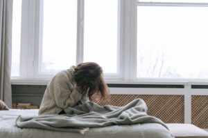 Erschöpfte Frau sitzt morgens auf dem Bett und stützt den Kopf in die Hand