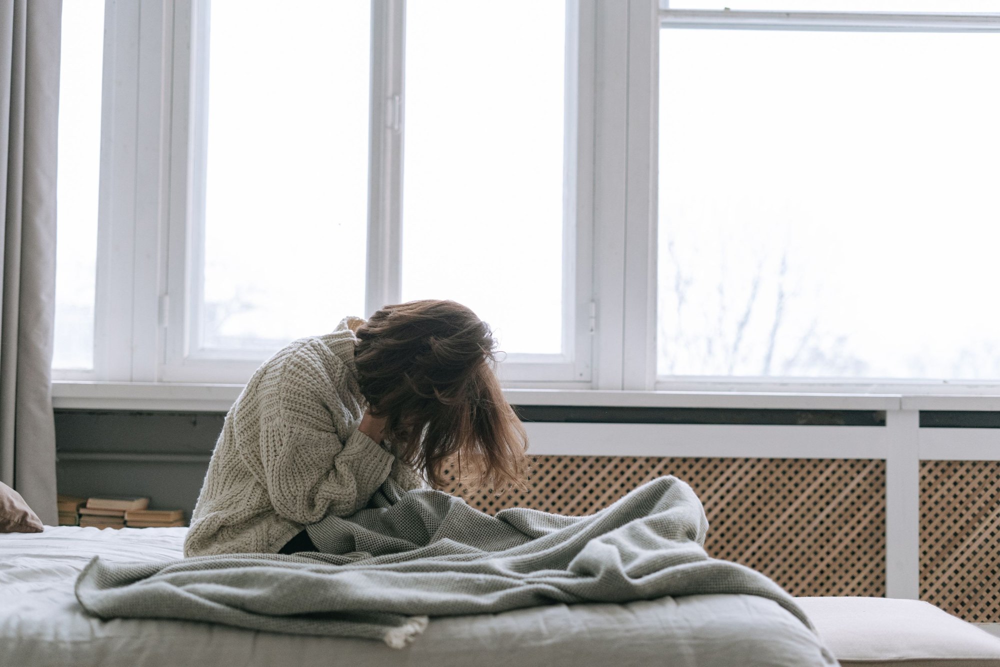 Erschöpfte Frau sitzt morgens auf dem Bett und stützt den Kopf in die Hand